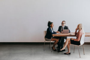 Two woman and a man sitting around a small table discussing performance review and development.
