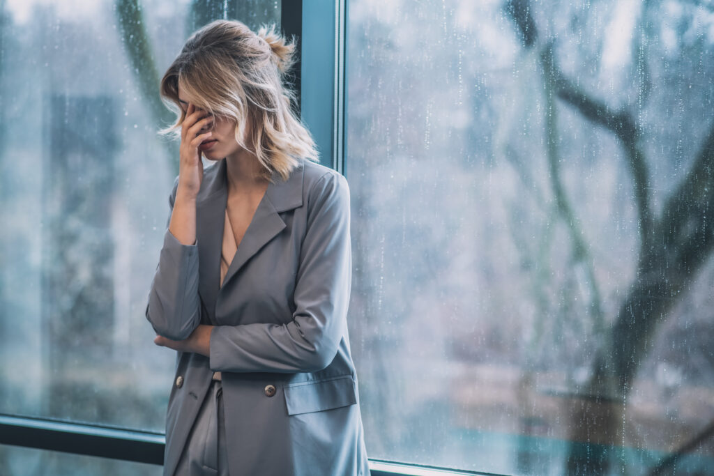 Woman covering her face with hand near window